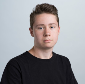 Ung person med kort hår i en svart skjorta, mot en vanlig ljus bakgrund.