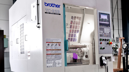 Industriell CNC-maskin märkt "Brother TC-R2B" med digitala kontroller, knappar och en bildskärm. Maskin i en ren verkstadsmiljö.