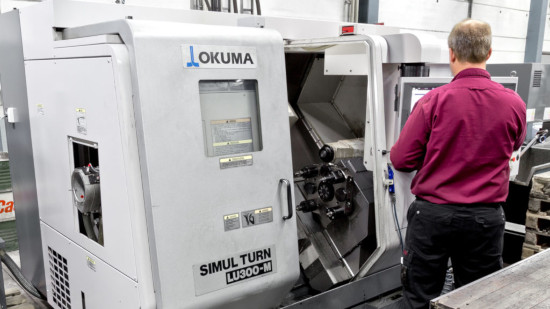 Person som använder en grå Okuma Simul Turn LU3000-EX-maskin i en verkstad.