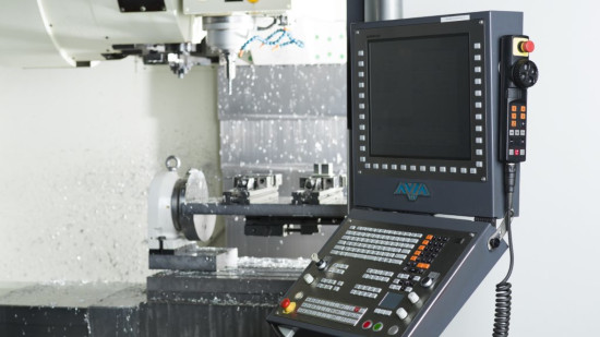 Industriell CNC-maskin med kontrollpanel i förgrunden, med skärm och olika knappar. Bakgrunden visar maskineri i drift med metallspån.